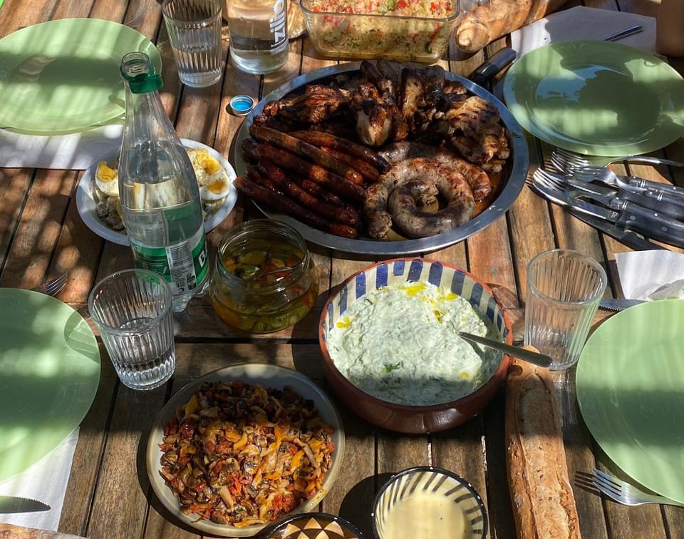 Grillades, saucisses, salades et pain partagés sur une table en bois en plein air